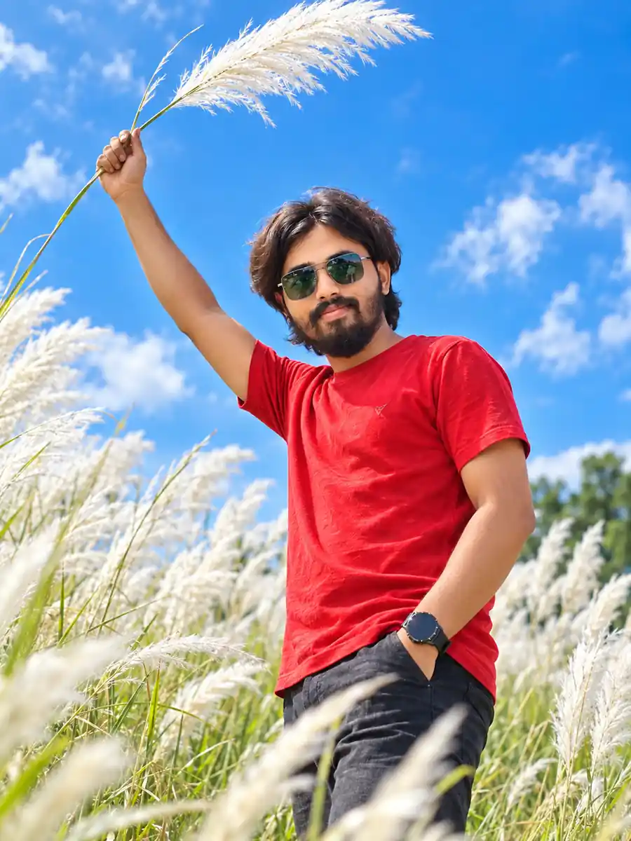 Young man in red shirt holding Kash flowers under blue sky